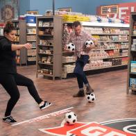 Host Guy Fieri looks on as contestants Antonia Lofaso and Brian Malarkey attempt to shoot goals with soccer balls, as seen on Guy's Grocery Games, Season 20.