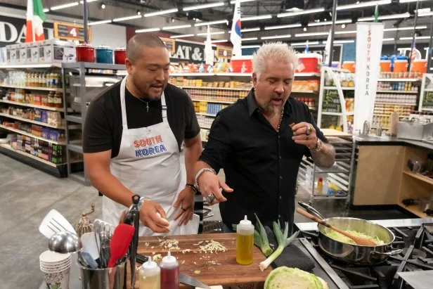 Host Guy Fieri checks on contestant Kevin Lee while he prepares his ingredients, as seen on Guy's Grocery Games, Season 41.