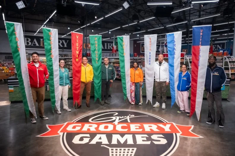 Contestants Gabe Bertaccini, Claudette Zepeda, Viet Pham, David Viana, Aarthi Sampath, Kevin Lee, Einat Admony, and Tobias Dorzon with flags for the countries they are representing, as seen on Guy's Grocery Games, Season 41.