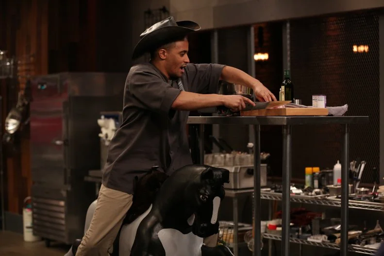 Chef Michael Jenkins works with a sabotage that forces him to forfeit his prep station and do all his prep sitting on a child's spring horse, as seen on Food Network's Cutthroat Kitchen, Season 9.