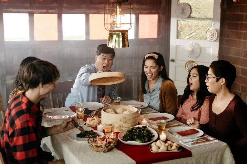 Host Molly Yeh's dad lifts the lid on a dishat the dining table. 
