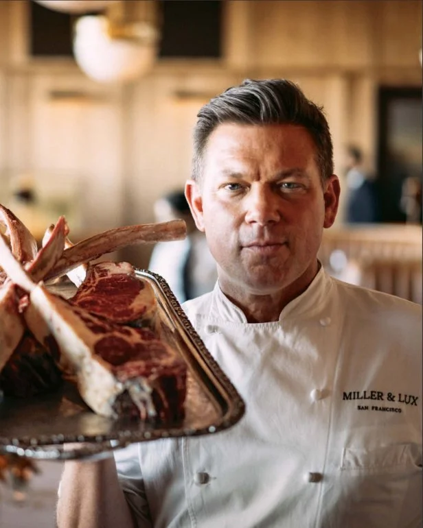 Chef Tyler Florence in a chef coat, holding a vintage metal tray of frenched ribs, at his Miller & Lux restaurant.