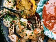 A platter of Tyler Florence's grilled shrimp cocktail with grilled lemons, plated with a blue and white bowl of cocktail sauce.