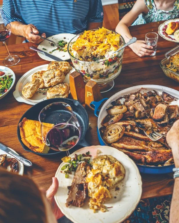 A spread of various dishes on a wooden table, hands dig into the dishes.