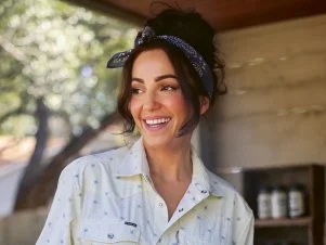 Jess Pryles moves meat with tongs over an open-fire grill in an outdoor kitchen. 