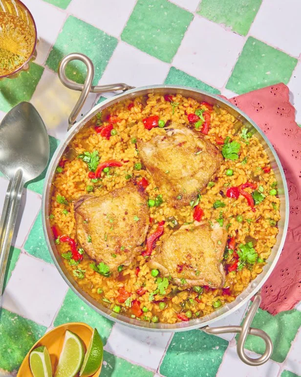 Mika Leon's  Arroz con Pollo a la Chorrera, a chicken thigh and rice dish plated inside a double handled metal dish, on a green-and-white checkered tablecloth.