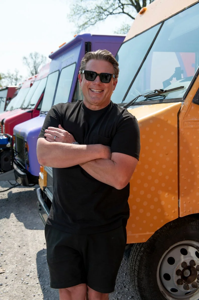 host Tyler Florence leans against a food truck with crossed arms
