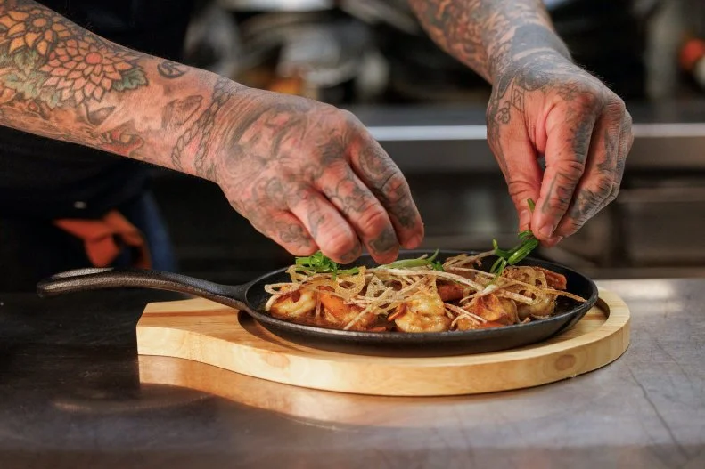 Aaron Sanchez plating Crispy Tofu with Sambal–Lime Glaze, Fried Taro Root & Herb Salad Sichuan Butter Shrimp dish in kitchen