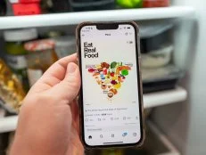 Illustrative image, close-up of a person's hand holding an iPhone displaying a social media post from the US Department of Health and Human Services showing the revised Food Pyramid with caption Eat Real Food, above the refrigerator in a domestic kitchen, Lafayette, California, January 7, 2026. (Photo by Smith Collection/Gado/Getty Images)