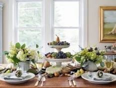 A symmetrical arrangement for the table’s focal point makes a visually strong statement.  In this case, the tall, stacked centerpiece is flanked with two bouquets that were made with the same flowers and produce in vases that are the same size and color.