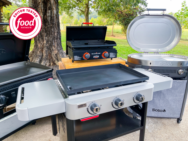 Four flat-top grills arranged together outside on concrete with the lids open and green grass in the background