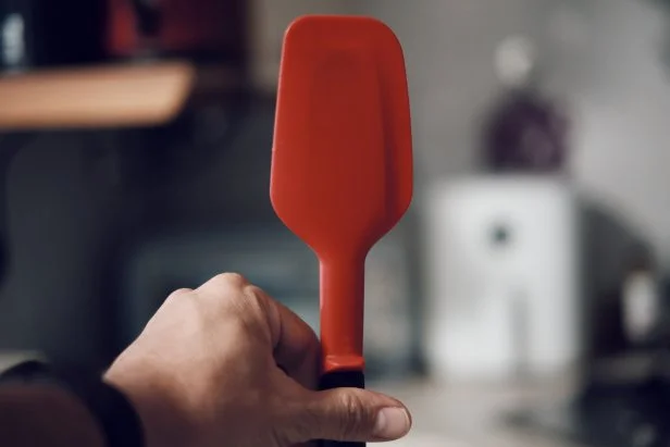 Silicone spatula, hand-held kitchen utensil, interior kitchen environment.
