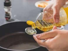 Cook pouring oil into a hot black saucepan