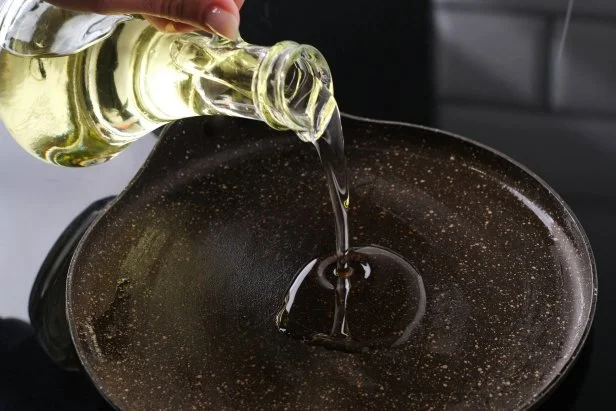 Girl Drizzling Oil Into A Heated Pan
