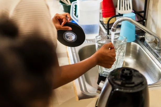 Woman filling blender with water in a kitchen sink, getting ready to prepare a meal