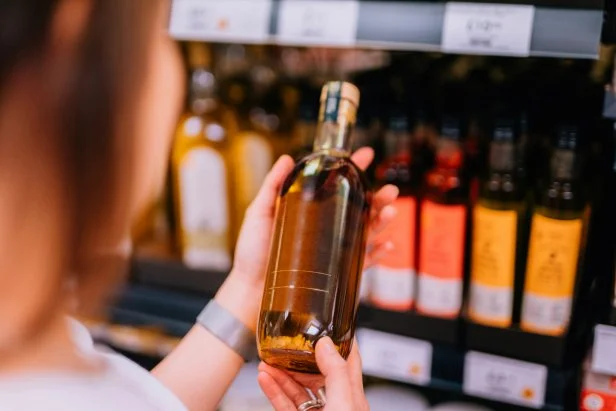 Over the shoulder view of young woman holding a bottle of olive oil against the shelf. Healthy eating and lifestyle.