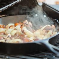 Step by step. Grilled mushrooms and onions in cast iron frying pan on outdoor gas grill.