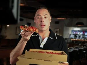 Behind the scenes of Jeff Mauro, holding a slice of pizza he looks very tempted to devour on location in Miami.