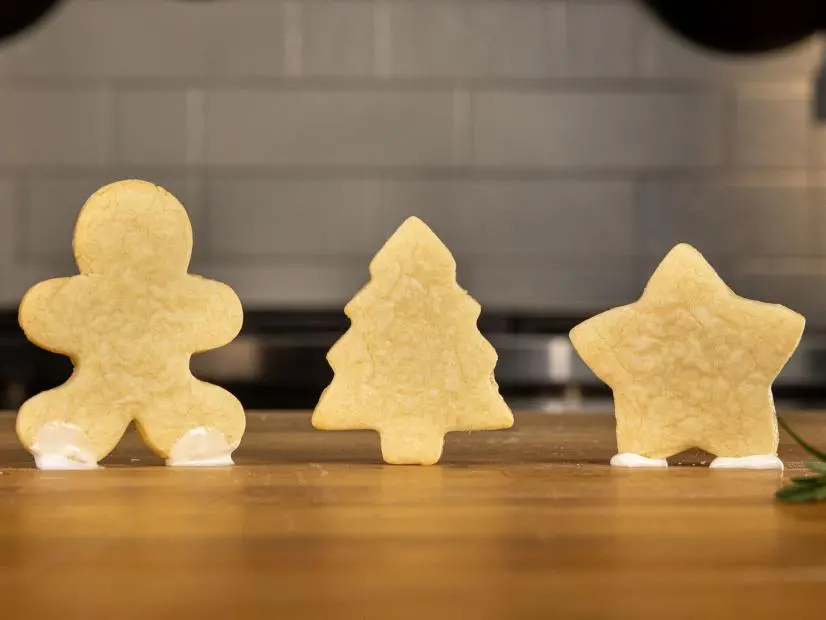 Sugar Cookies 2.0 in the shapes of a gingerbread man, a Christmas tree, and a star stand in a line on the counter of the Good Eats test kitchen, as seen on Food Network Kitchen's Alton Brown Holiday Classes, Season 2.