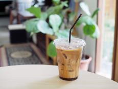 A plastic glass of iced coffee latte; upper layer is froth milk lower is brown bitter coffee on the wooden table with selective focus.