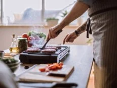 Young Male Chef Turning Sides Of Hamburgers On Electric Grill