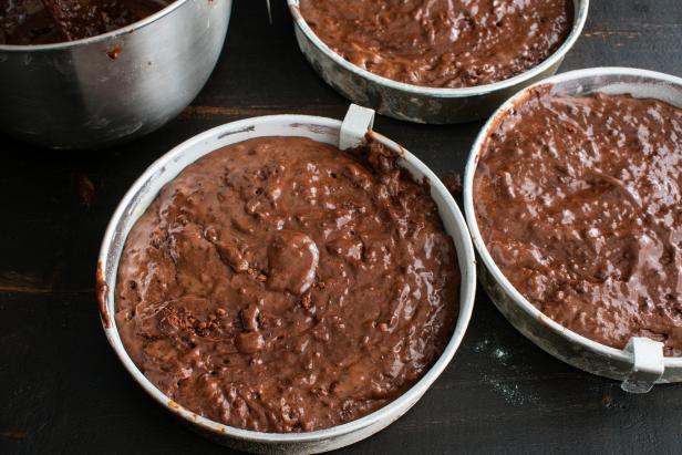 Three greased and floured aluminum cake pans filled with chocolate cake batter