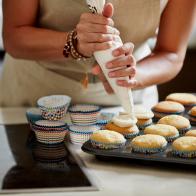 Midsection of woman icing cupcakes at kitchen counter