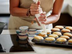 Midsection of woman icing cupcakes at kitchen counter