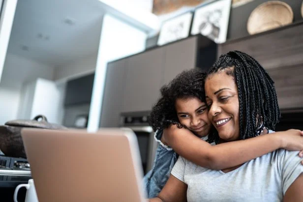 Mature woman working from home and being embraced by daughter