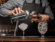Bartender pouring alcoholic drink into a glass using a jigger to prepare a fresh cocktail