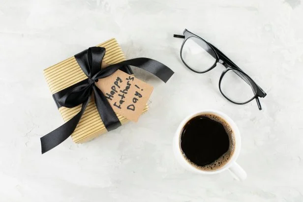 Glasses, coffee cup and craft present box on light background. Happy Father's Day concept. Greeting card. Top view, flat lay