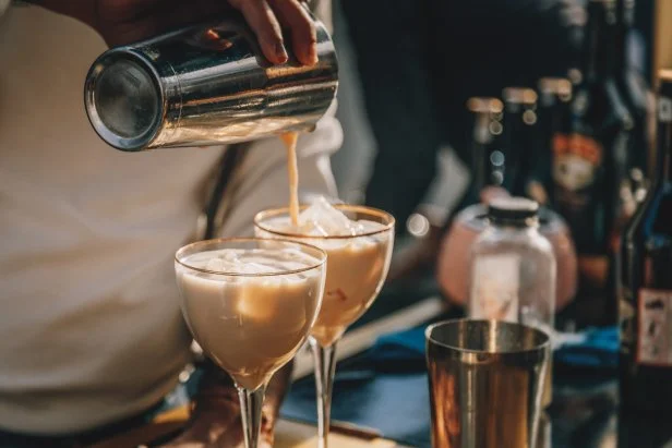 Close up male bartender hands making Baileys cocktail with ice and pouring to glass from bar shaker