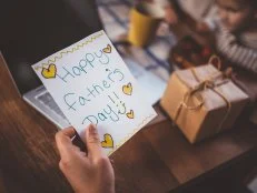Close-up of father's hands holding handmade card and present from children on father's day