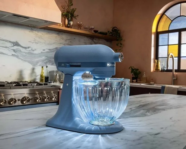 Light blue KitchenAid stand mixer on a marble countertop with an integrated light illuminating the glass bowl