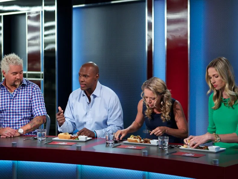 Host Guy Fieri with judges DC Crenshaw, Melissa D'Arabian, and Catherine McCord during the judging of Game 2, Closing Time, Ultimate Hot Dog, 2 min shopping and 30 min cooking time, as seen on Food Network's Guy's Grocery Games, Season 1.