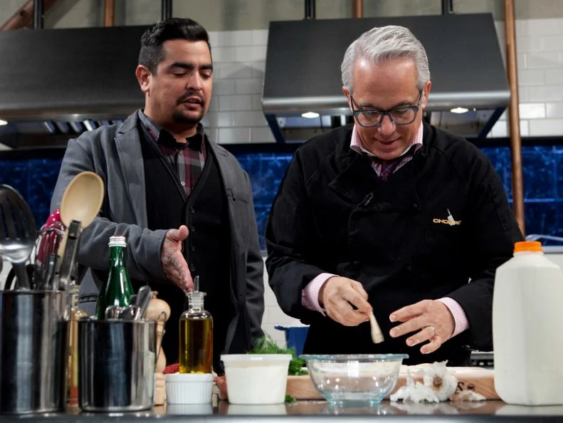 Chopped: After Hours host Aaron Sanchez talks to chef Geoffrey Zakarian while he is working on his entree that must include: deep dish pizza dough, rabbit escabeche, swiss chard and pineapple cheese spread, as seen on Food Network's Chopped: After Hours.