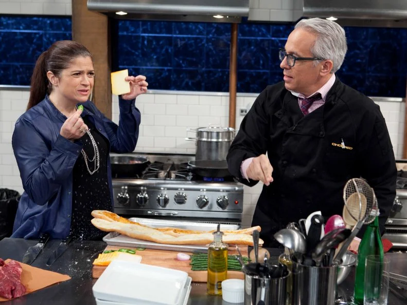 Chopped: After Hours host Alex Guarnaschelli talks to chef Geoffrey Zakarian about his choice in ingredients while he is working on his entree that must include: tikka masala sauce, Asian long beans, hanger steak and croquettes, as seen on Food Network's Chopped: After Hours.