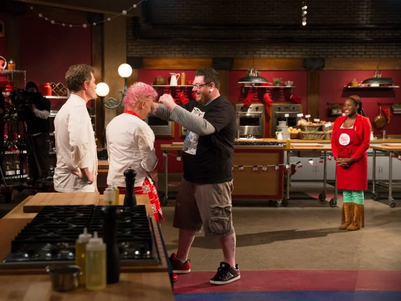 Host Bobby Flay watches as host Anne Burrell lets contestant Benji Brown touch her hair after he was from the competition as seen on Food Networkâ  s Worst Cooksin America, Season 5.