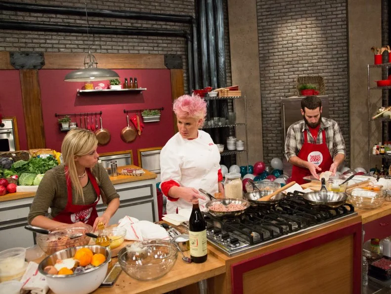 Red Team members Carie Pullano-Keller and Mike Glazer race to prepare their dishes with Red Team Leader Chef Anne Burrell standing close by, for the Surprise Party Challenge. They must replicate Red Team Leader Chef Anne Burrell's Chicken & Broccoli Rabe Summer Rolls and Sausage-Stuffed Mushrooms and infuse it with their individual surprise candy flavors, as seen on Food Network's Worst Cooks in America, Season 5.