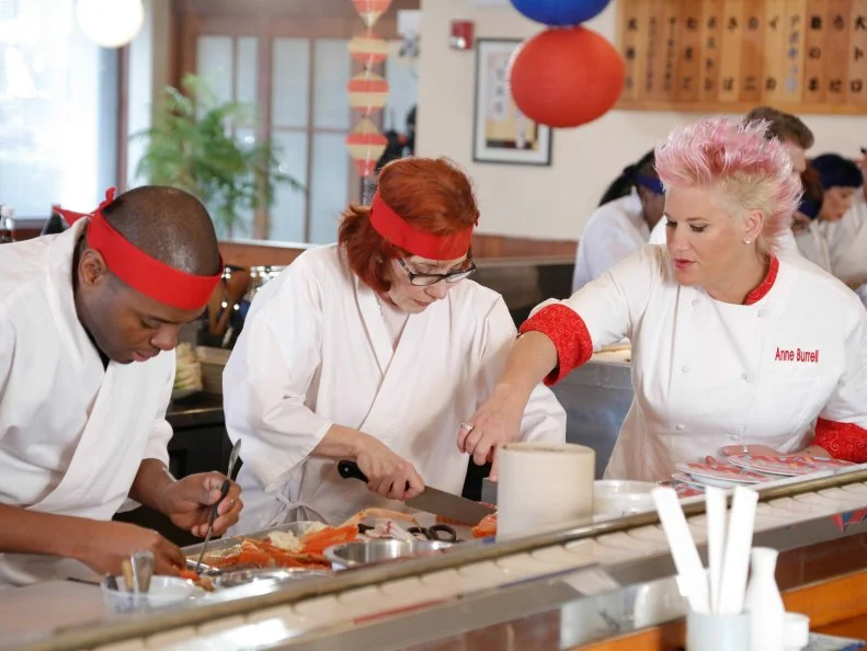 Chef Anne Burrell coaches Red Team members as they race to beat the clock during the Sushi Skill Drill Challenge. The Red and Blue team recruits must prepare two sushi dishes for a hungry lunchtime crowd and are tested on both their time & quantity: A California Roll with snow crab, nori, rice on the outside, garnished with sesame seeds and a Salmon Roll with sliced salmon, scallion, sushi rice, spicy mayo (with nori on the outside.)  The diners will determine which team will win the challenge, as seen on Food Network's Worst Cooks in America, Season 5.