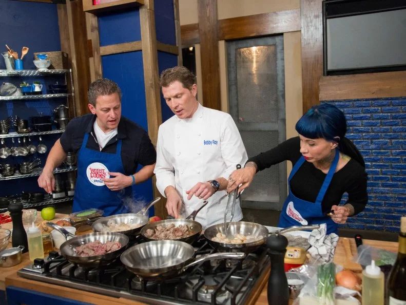 Blue Team Leader Chef Bobby Flay surveys the progress of Blue Team members Daniel Beyda and Amber Brauner during the Surprise Party Challenge. The Blue Team must replicate Blue Team Leader Chef Bobby Flay's recipe for Shrimp and Brussels Sprouts Spring Rolls with Sesame Ginger Dipping Sauce and Raw Tuna-Stuffed Piquillo Peppers, and infuse it with their individual surprise candy flavors, as seen on Food Network's Worst Cooks in America, Season 5.