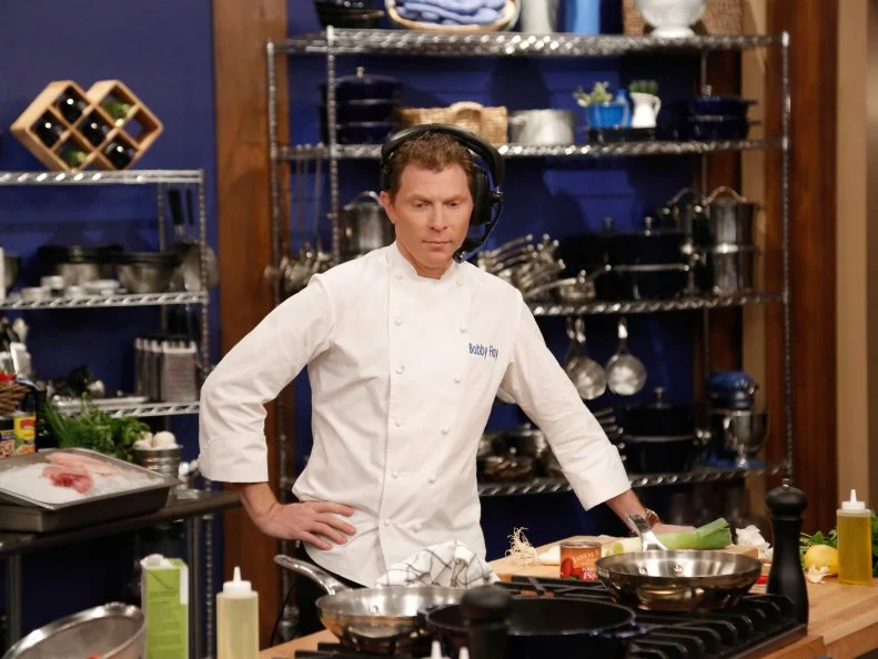 Blue Team Leader Chef Bobby Flay listens to his team try to nail down the ingredients in their Halibut with Endive and Gremolata, during the Remote Control Skill Drill. The Blue Team, Daniel Beyda and Amber Brauner, must direct him via headset to make the same dish they are seeing for the first time, as seen on Food Network's Worst Cooks in America, Season 5.
