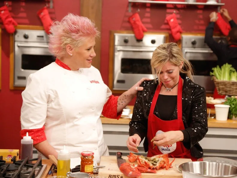 Chef Anne steps in to check Red Team member Carie Pullano-Keller's progress during the Surf and Turf Challenge. Each team must replicate a steak and lobster dinner from scratch, demonstrated to them by their team leader; Grilled Ribeye with Fra Diavolo Lobster Relish by Chef Bobby Flay for the Blue Team, and Dry Rubbed Rib Eye with Chili Lobster by Chef Anne Burrell for her Red Team, as seen on Food Network's Worst Cooks in America, Season 5.