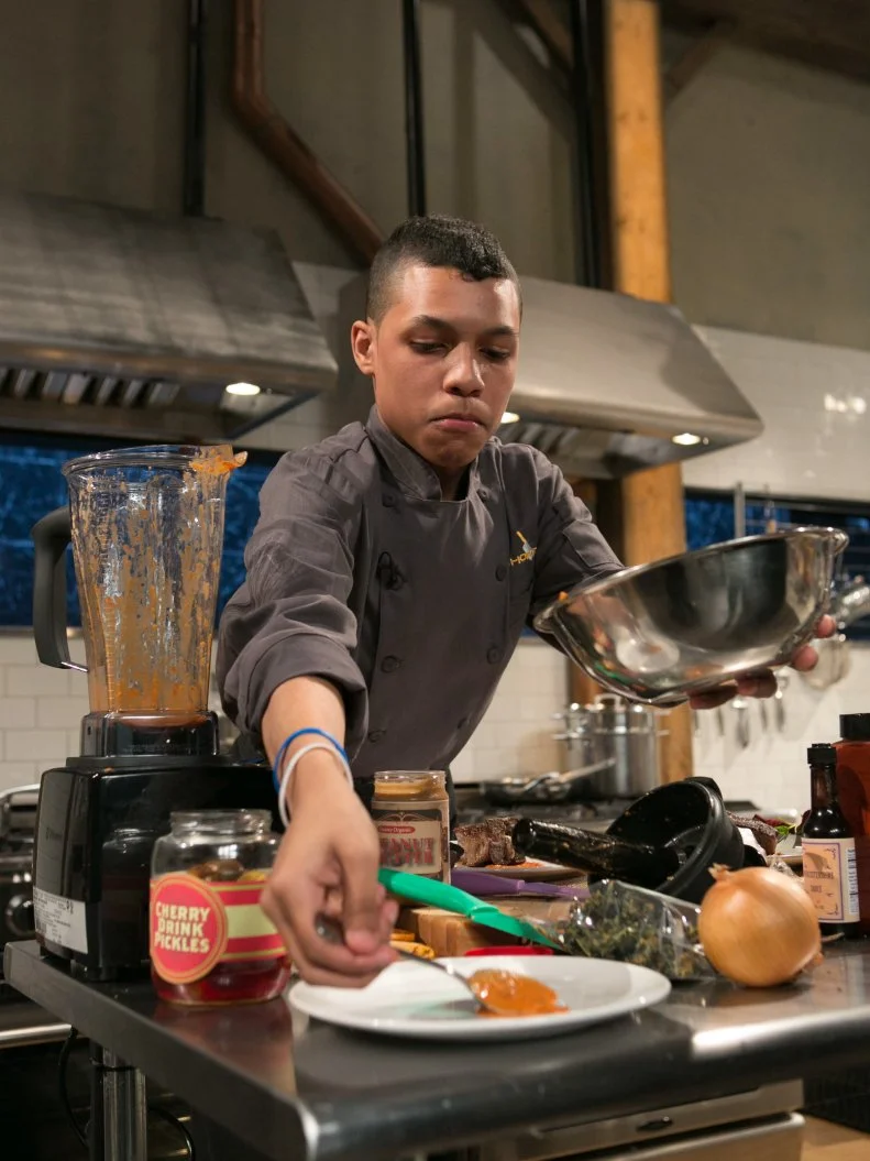 Teen Competitor Jay Urena (16) working on his appetizer that must include: cherry-drink-soaked pickles, lamb loin chops, kale chips and ricotta salata, as seen on Food Network's Chopped, Season 21.