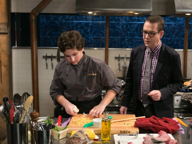 Chopped host Ted Allen checks in with teen competitor Jason Khaytin (14) as he works on his entree that must include: mahi-mahi, cookie chips, green beans and french fries, as seen on Food Network's Chopped, Season 21.