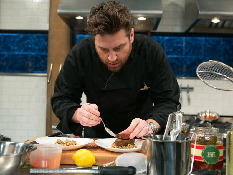 Chef Scott Conant works on his dish that must include:cherry drink soaked pickles, lamb chops, kale chips and ricotta salata, as seen on Food Network's Chopped After Hours, season 21.
