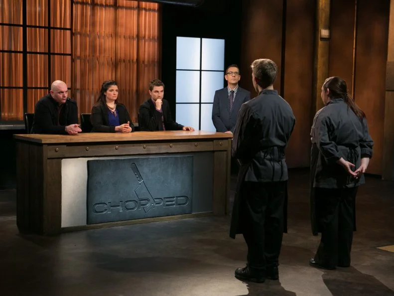 Teen competitors Tommi Rae Fowler (16) Max Aronson (16) stand before host Ted Allen and judges: Chris Santos, Alex Guarnaschelli and Alex Stupak to defend their desserts that must have included: chocolate fudge, cinnamon cereal , pie crust and grape-flavored carbonated candy as they compete for a slot in the Teen Challenge and a chance to win $25,000 and a $40,000 culinary school scholarship, as seen on Food Network's Chopped, season 21.