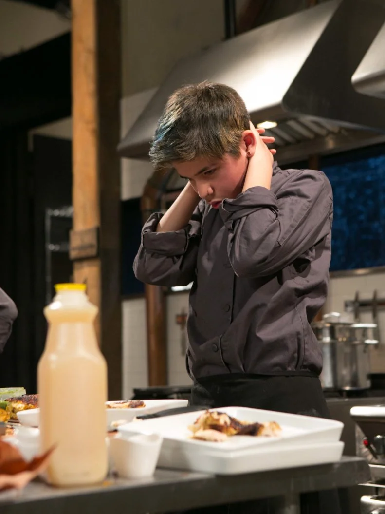 Teen competitor Antonio Jubela Gordon (16) looks down on his plates after finishing his appetizer that must have included: salsa verde, chicken breast, bundled lunch kits and blue corn tortilla chips as he competes for a slot in the Teen Challenge and a chance to win $25,000 and a $40,000 culinary school scholarship, as seen on Food Network's Chopped, season 21.