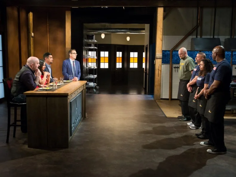 Hero Champions Robbie Myers, Paul Rut, Diana Sabater, and Richard Fields stand before Judges Chris Santos, Maneet Chauhan, Aaron Sanchez and Host Ted Allen during judging, as seen on Food Networkâ  s Chopped, Season 21.