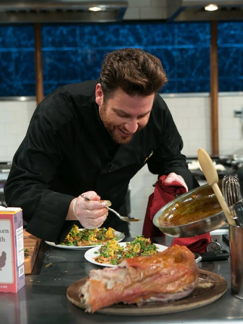 Chef Scott Conant jokes with the camera while he works on his dish that must include: whole suckling pig, kebab sauces, fiddlehead ferns and fresh corn tortillas, as seen on Food Network's Chopped After Hours, Season 21.